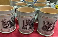 Eight Denby stoneware mugs showing gray glaze with gold trim and different black village scene illustrations.