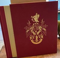 Close-up of the red hardcover book with gold embossed crest and detailing.