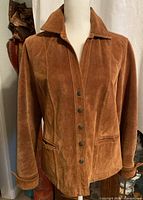 Front view of brown suede leather ladies jacket with snap buttons and two pockets.