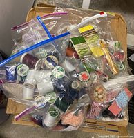 Top view of box containing multiple resealable bags filled with colorful spools of thread, lace scraps, and sewing tools.