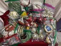 Overview of many Christmas ornaments in plastic bags showing baubles, fabric figures, and other holiday shapes on a red cloth.
