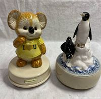 Photo of both vintage Otagiri ceramic musical figurines: Koala and Penguins side by side on a white background.