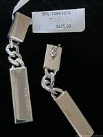 Close-up of earrings highlighting the engraved 'PIANEGONDA' on rectangular silver ingots and original price tag from Neiman Marcus.
