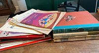 Stack of various colorful and vintage piano sheet music and books on a wooden table