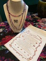 Front view of necklace on bust, butterfly brooch pinned below strands, poem printed sheet beside bust.