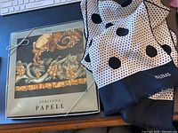 Photo of Adrianna Papell silk scarf in original packaging alongside folded Bill Blass polka dot scarf on a desk.