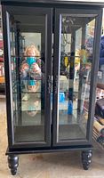 Front view of tall black wood curio cabinet with glass doors and shelves inside.