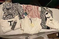 Six women's clothing items including flowy pants and tops arranged on a surface. Some with tags, multiple patterns and light-weight fabrics.