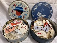 Two vintage decorative tins filled with assorted buttons and sewing notions in original packaging and blister packs.