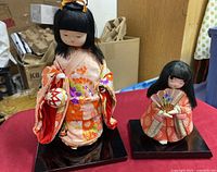 Both vintage Geisha dolls shown side by side on black bases with detailed kimono clothing and accessories.