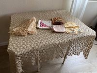 Ecru crocheted tablecloth spread on table with assorted napkins on top including floral, plain, and embroidered ones.