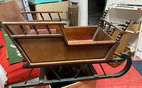 Side angle view of the large vintage wooden handmade sleigh showing the turned spindle armrests, wooden body, and metal runners.
