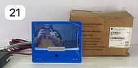 Blue 7-inch color monitor with protective screen film and box in background showing product details.