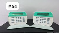 Two white and teal Tyco security keypads with LCD displays seen from the front with covers open, keypad buttons visible, showing they are hardwired alarm control panels.