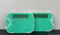 Two teal and white Tyco security keypads with LCD screens, front view closed.