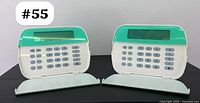 Front side of two Tyco security alarm keypads with numeric buttons and LCD screens visible, positioned upright on a black surface.