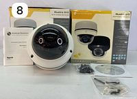 Two American Dynamics Illustra 610 HD IP mini dome cameras with original boxes, one camera visible outside box, dome camera shape with tinted domes visible, manufacturer branding on boxes.