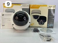 Two American Dynamics Illustra 610 Mini Dome Cameras front view with boxes, instruction manuals, quick start guides, and mounting hardware in front.