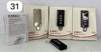 Three DSC wireless 4-button remote controls in original packaging with one out of package, showing front buttons and labels.