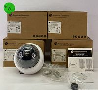 Four American Dynamics camera boxes stacked with one white indoor dome camera, clear bubble, model label visible, accessories and manual included.