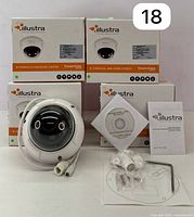 Four Illustra Essentials IP varifocal mini-dome cameras in boxes with one camera outside and visible mounting hardware, quick start guide, and installation CD.