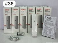 Six DSC PowerG Wireless Shock Sensor units in their boxes with one sensor outside, battery, mounting screws, and manual laid out.