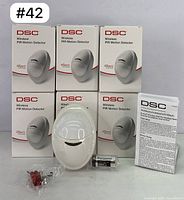 Six boxed DSC Wireless PIR Motion Detectors PG8904P with one sensor, battery, screws, and manual outside the boxes, showing the full lot contents.
