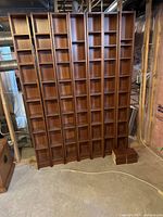 Seven narrow bookcases arranged side by side in an unfinished basement area