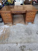 Front view of large antique solid wood desk with brass drawer pulls and multiple drawers.