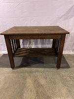 Full front view of the antique solid wood table showing the vertical slat design on the sides, lower shelf, and wheels on legs.
