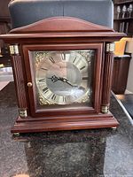 Front view of Bulova wooden mantel clock with silver Roman numeral clock face, decorative gold corners, and fluted side columns.