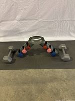 Full view of the weight set showing pairs of 1,2,3 lb neoprene dumbbells in red, pink, blue colors and two gray 15 lb hex dumbbells on a black mat.