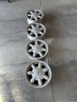 Four silver Mazda alloy wheels laid out on concrete floor showing 7-spoke design and condition of all wheels.
