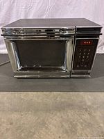 Front full view of first generation Amana microwave oven showing metal finish with chrome accents and door with grid window.