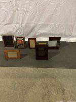 Eight assorted stand-up picture frames in various wood finishes and sizes, arranged upright to display front views.