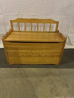 Front view of the solid wood storage bench with decorative carved floral panel and spindled backrest