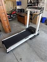 Full side and angled view of the white Spirit SmartSpace treadmill in a garage setting, showing its frame, running belt and part of the folded mechanism.