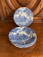Six blue and white plates depicting Anne Hathaway's Cottage arranged on wooden furniture.