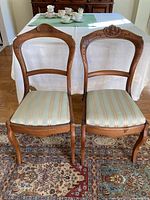 Front view showing both antique chairs side by side with striped upholstered seats and carved wooden backs.