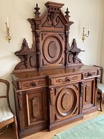 Front view of two-piece carved oak sideboard showing three drawers above three cabinet doors and top crest