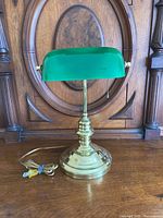Front view of the bankers lamp showing the green glass shade and brass base with power cord.