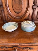 Photo showing the set of two hand-thrown pottery dishes on wood surface against wood background, bowl on left, casserole dish with lid on right.