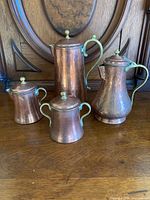 Complete set of copper coffee and tea pieces with lids and handles, showing hammered texture and greenish patina.