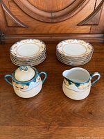 10 dessert plates stacked in two piles with a cream and sugar set placed in front, showing pattern and size