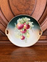 Full front view of the round porcelain plate with hand painted apples and gradient green to white background, showing the design and two side handles.