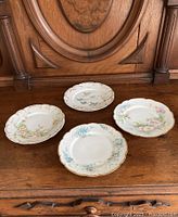 Four hand-painted floral porcelain plates placed on wooden surface, showing overall lot contents