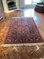 Full view of Persian style medium rug with fringe lying flat on wooden parquet floor near fireplace and chair.
