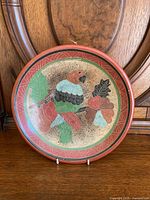 Front view of round Mexican pottery bowl featuring colorful parrot and floral painted design with red border.