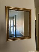 Full view of the rectangular brass-colored framed wall mirror hanging on a wall.