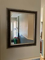 Full view of the silver-colored rectangular mirror hung on a wall reflecting a hallway and doorway.